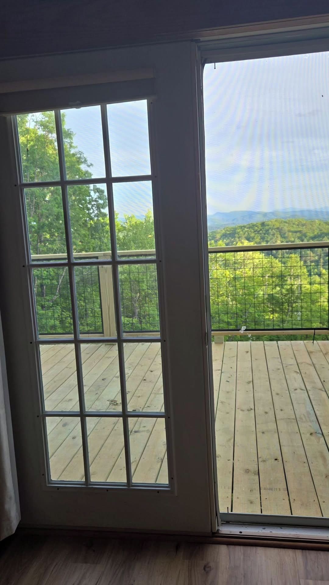 A room with a large sliding glass door leading to a wooden deck with a view of a green landscape.