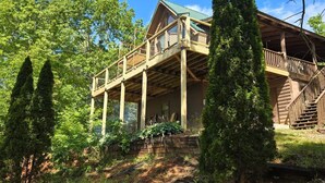 Eine Holzhütte mit Balkon, umgeben von Bäumen und wolkenlosem Himmel.
