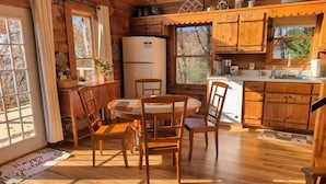 Ein Holzblockhaus-Interieur mit Esstisch, Stühlen, einem Kühlschrank und einer Küchenzeile.