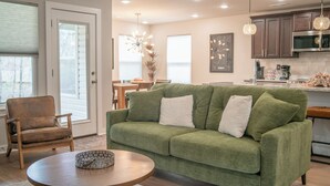 Ein modernes Wohnzimmer mit einem grünen Sofa, einem Holztisch und einem Essbereich mit Tisch und Stühlen.