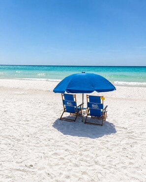 Una playa con dos sillas azules y una sombrilla azul bajo un cielo despejado.