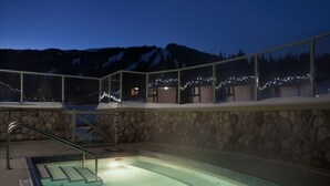 Un jacuzzi con paredes de piedra y barandilla de cristal con vistas a una montaña nevada.