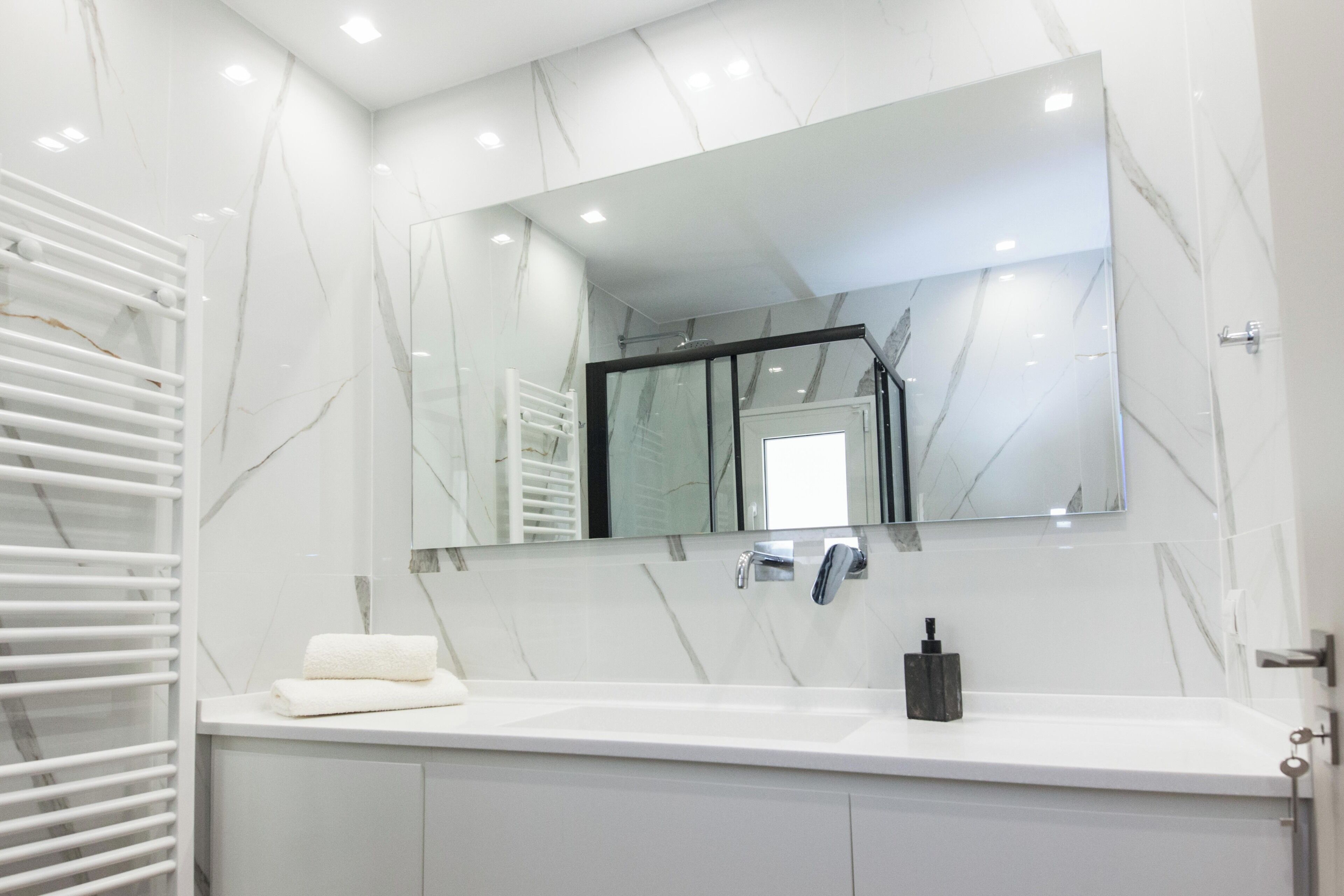 Une salle de bain moderne avec un comptoir en marbre blanc, un grand miroir et un porte-serviettes.