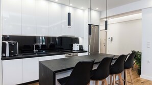A modern kitchen with white cabinets, a black countertop, and black bar stools. - Athens Riviera 2BR Apartment by ΜΡS (Kallithea)