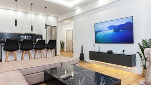 A modern living room with a large TV, a marble coffee table, and a seating area with a sofa and chairs. - Athens Riviera 2BR Apartment by ΜΡS (Kallithea)