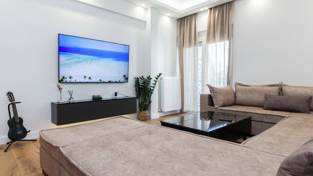 A modern living room with a large flat-screen TV, a sofa, a coffee table, and a guitar. - Athens Riviera 2BR Apartment by ΜΡS (Kallithea)