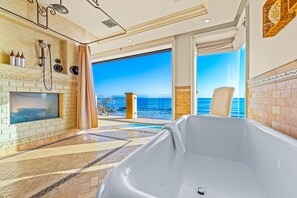 Une salle de bain avec une baignoire, une douche et une grande fenêtre donnant sur l’océan.