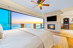 Une chambre avec un grand lit, un ventilateur de plafond, une cheminée, une télévision et une vue sur l’océan.