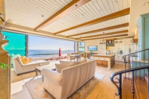 Un vaste espace de vie avec une grande fenêtre donnant sur l’océan, une cuisine dotée de meubles blancs et un escalier avec une rampe.