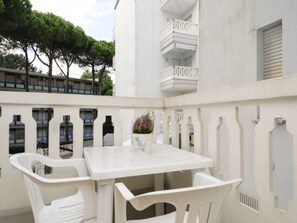 A white outdoor seating area with a table and chairs, a potted plant, and a balcony with railings. - Cozy Accommodation With Shared Pool (Lignano Sabbiadoro)
