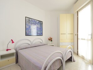 A bedroom with a bed, bedside table, lamp, artwork, and a wardrobe. - Cozy Accommodation With Shared Pool (Lignano Sabbiadoro)