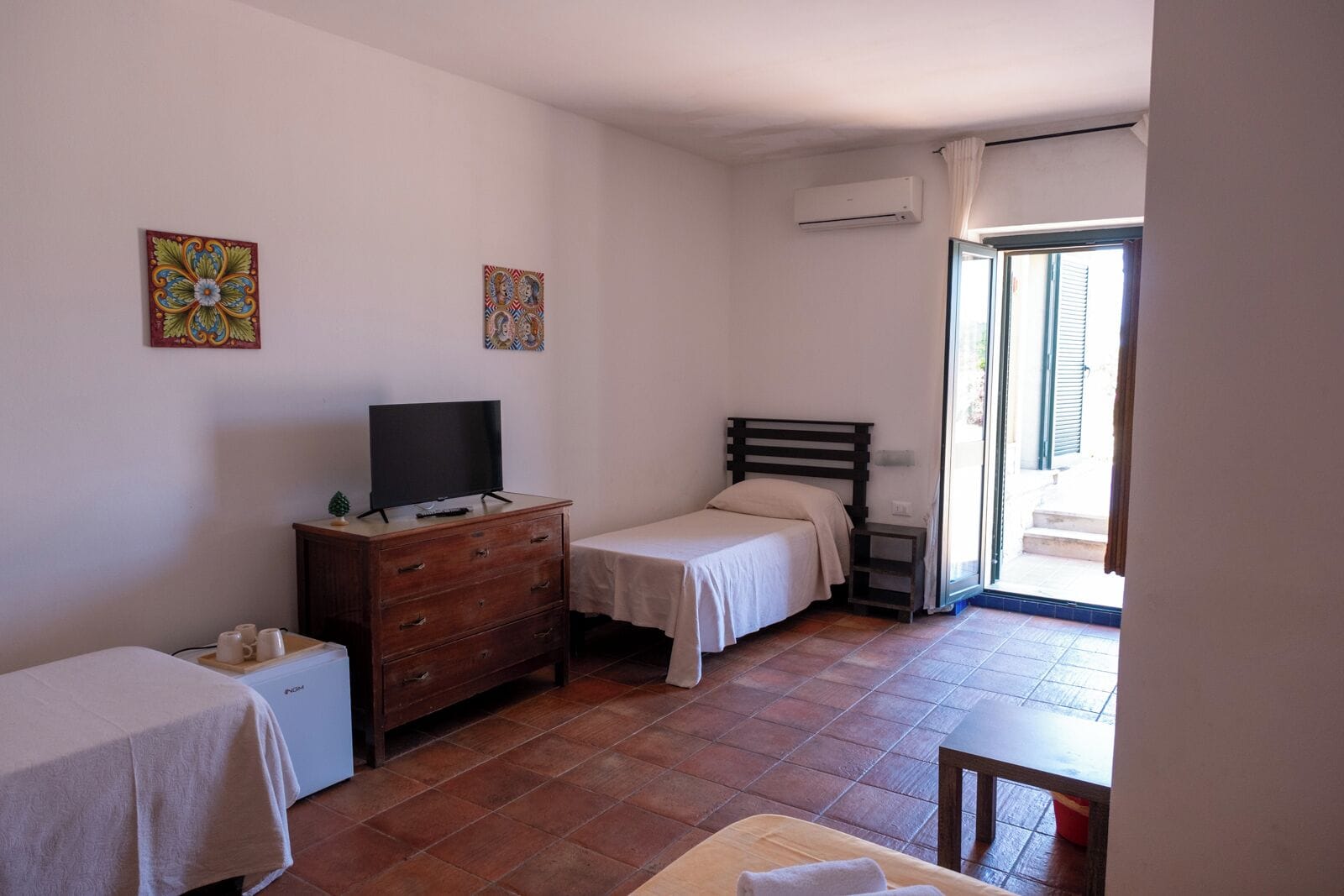 A bedroom with two beds, a TV on a dresser, and an air conditioning unit.