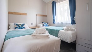 A hotel room with two beds, a wooden headboard, a window with blue curtains, and a bedside table with a towel.