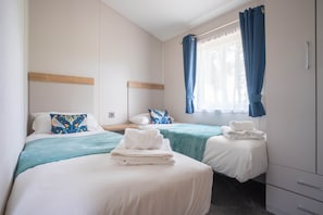 Une chambre d’hôtel avec deux lits, une tête de lit en bois, une fenêtre avec des rideaux bleus et une table de chevet avec une serviette.