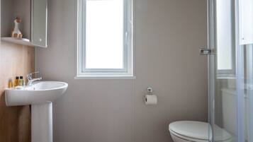 A bathroom with a white sink, a toilet, a window, and a shower enclosure.