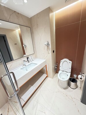 A modern bathroom with a dual sink vanity, a toilet, a bidet, and a trash bin.
