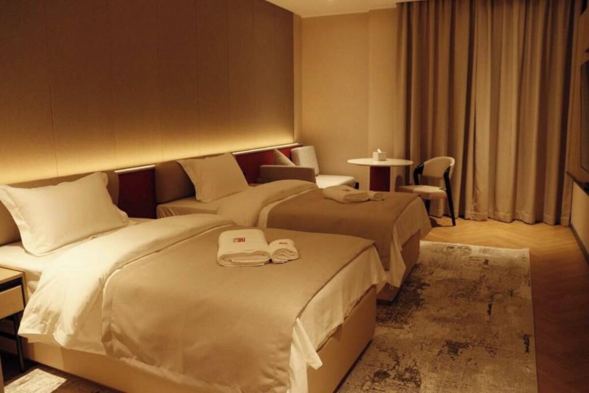 Hotellihuone, jossa on kaksi sänkyä, pieni pöytä, tuoli ja näkymä ulos.