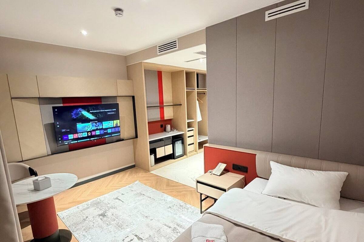 Moderni hotellihuone, jossa on sänky, työpöytä, televisio ja vaatekaappi.