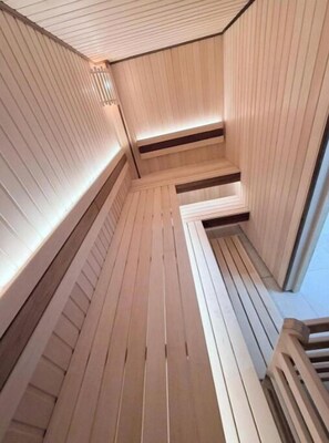 Uma sauna com paredes e bancos de madeira, piso inclinado e claraboia.