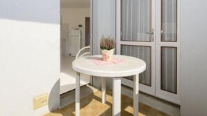 Una pequeña mesa redonda blanca con una planta en maceta en el centro, ubicada en una habitación con puerta corredera de vidrio y pared blanca.