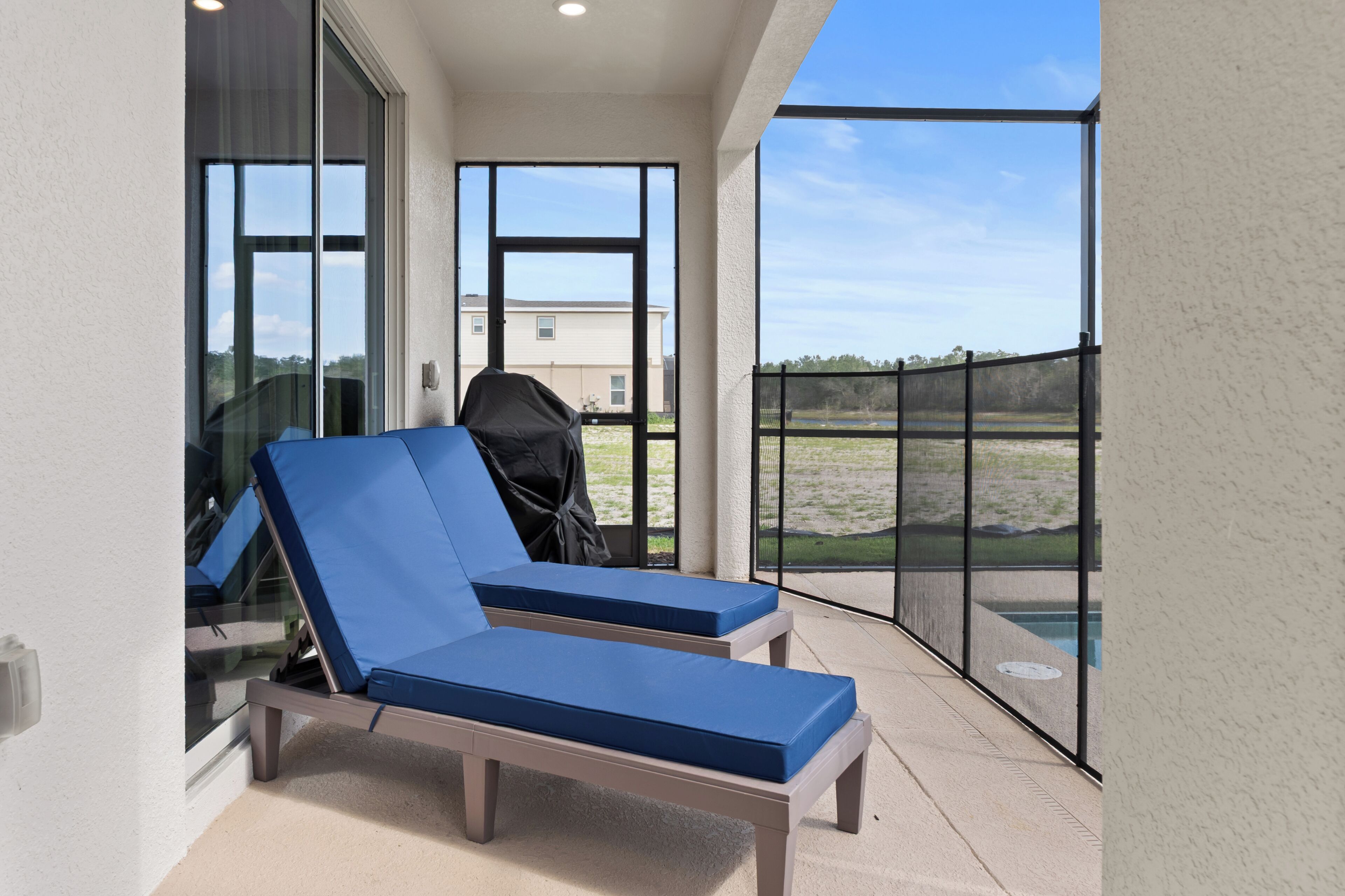 Un balcon avec deux fauteuils bleus, un barbecue et une vue sur une piscine et des bâtiments éloignés.