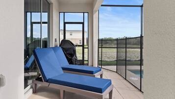 Un balcon avec deux fauteuils bleus, un barbecue et une vue sur une piscine et des bâtiments éloignés.