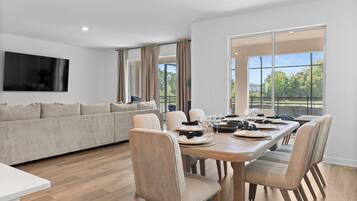 Un salon moderne avec un canapé, une table à manger pour quatre personnes et un téléviseur fixé au mur.
