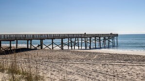 En træbro, der strækker sig ud i havet, med folk, der går langs den.