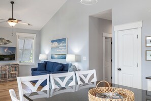 Ein modernes Wohnzimmer mit einem blauen Sofa, weißen Stühlen, einem Glastisch und einem Deckenventilator.