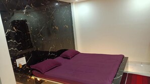 A bed with a purple bedspread and pillows, a marble wall, and a red rug. - Hotel HCB (Brahmapur)