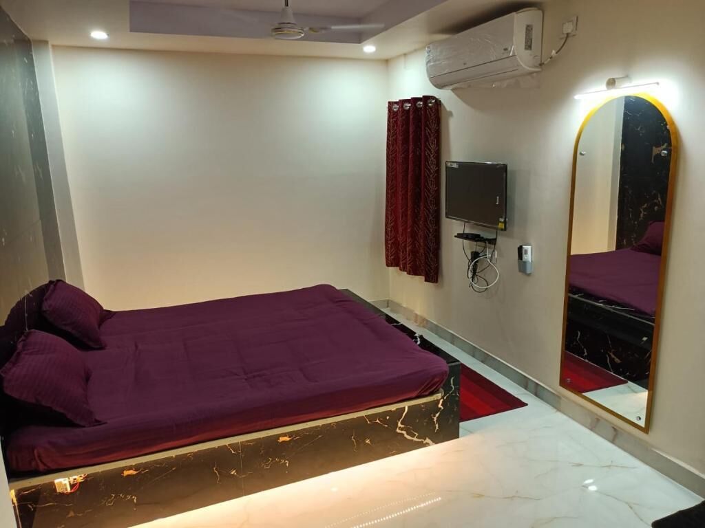 A bedroom with a bed, a television, a mirror, and an air conditioning unit.