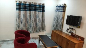 A living room with a TV, a wooden cabinet, and red chairs. - Hotel HCB (Brahmapur)