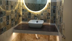 A bathroom with a round mirror, a sink, tiled walls, and a shower area. - Hotel HCB (Brahmapur)