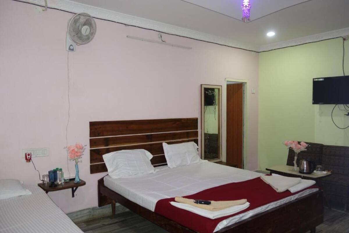 A hotel room with a bed, bedside table, mirror, TV, and a fan.