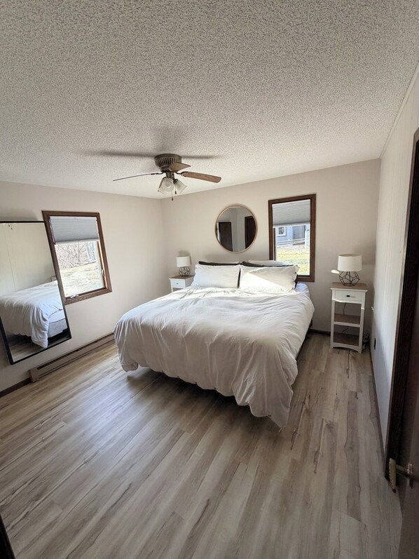 Une chambre à coucher avec un lit, un ventilateur de plafond, un miroir rond, des tables de chevet et une fenêtre.