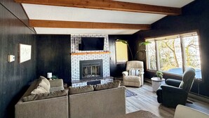 A living room with a fireplace, wooden beams, a sofa, a chair, and a window with a view. - Lake Carlos Getaway w/Sandy Beach, Dock, Lift & Stunning Sunsets 3-bedroom house (Carlos)