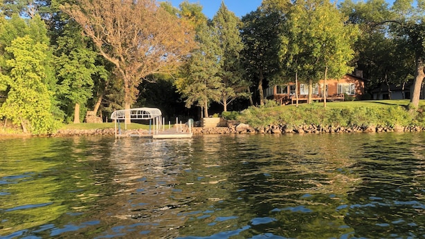 A serene lakeside view with a gazebo, trees, and a house in the background. - Lake Carlos Getaway w/Sandy Beach, Dock, Lift & Stunning Sunsets 3-bedroom house (Carlos)