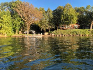 Une vue paisible sur un lac, avec un belvédère, des arbres et une maison en arrière-plan.