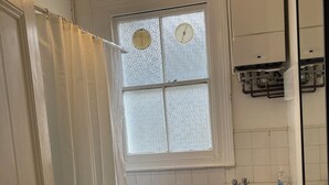 Un baño con bañera, lavamanos, ventana con vidrio esmerilado y un perchero para toallas.