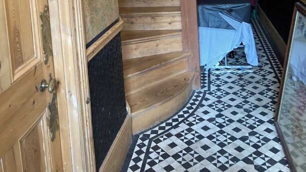 Una escalera de madera con un candelabro, un suelo con estampado y pisos de cerámica.