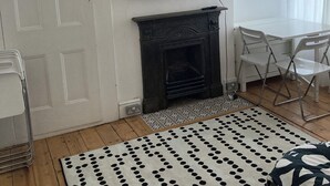 Una sala de estar con una televisión de pantalla plana en la pared, chimenea, sillas blancas, alfombra estampada y una puerta.