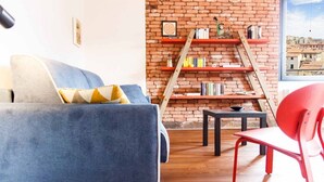 Una sala de estar con un sofá azul, un sillón rojo, un muro de ladrillo y una estantería.