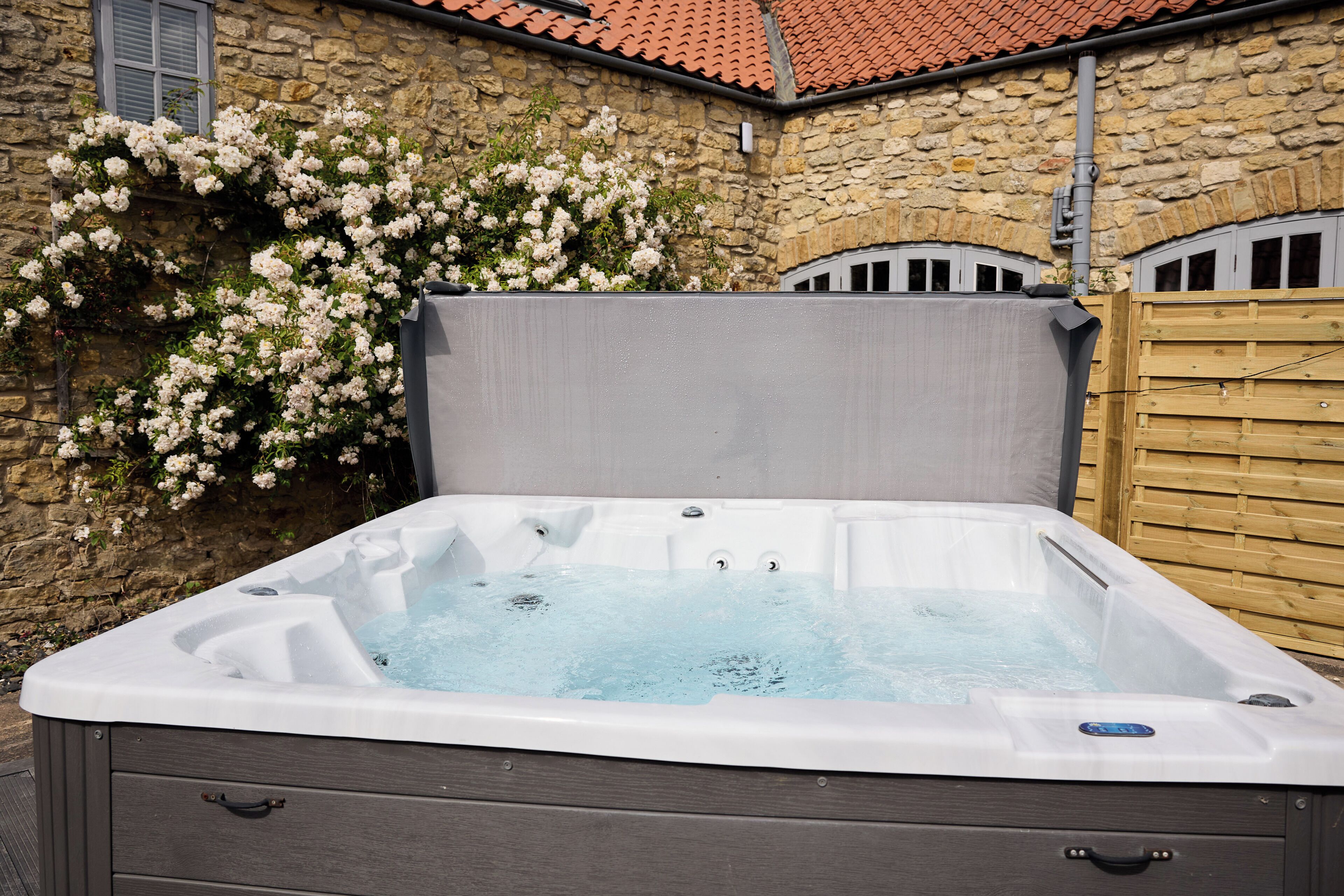 A hot tub with a wooden deck, stone walls, and a tiled roof. - Jasmine Cottage | Sands Farm (Wilton)