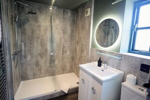 A modern bathroom with a glass-enclosed shower, a white sink, and a round mirror. - Jasmine Cottage | Sands Farm (Wilton)