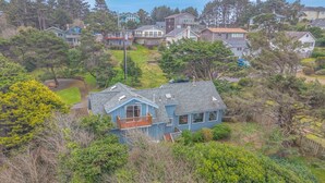 A residential house with a balcony, surrounded by dense greenery and other houses in the background. - Lincoln City Retreat: Private Hot Tub, Game Room, Easy Beach Access (Lincoln City)