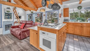 A modern kitchen with wooden cabinets, a built-in oven, and a dining area with a red leather sofa. - Lincoln City Retreat: Private Hot Tub, Game Room, Easy Beach Access (Lincoln City)