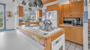 A modern kitchen with wooden cabinets, a large island with a kettle, and a microwave. - Lincoln City Retreat: Private Hot Tub, Game Room, Easy Beach Access (Lincoln City)