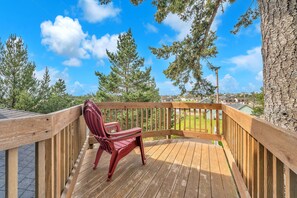 A wooden deck with a red chair, surrounded by trees and a clear sky. - Pacific City Oasis: Ocean Views, Game Room & Walk to Bob Straub Park (Pacific City)