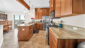 A kitchen with wooden cabinets, a granite countertop, a stainless steel refrigerator, and a built-in oven. - Pacific City Oasis: Ocean Views, Game Room & Walk to Bob Straub Park (Pacific City)