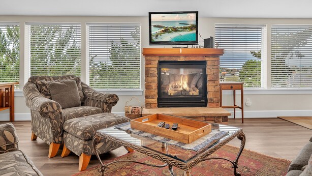 A living room with a fireplace, a sofa, a coffee table, and a TV mounted on the wall. - Pacific City Oasis: Ocean Views, Game Room & Walk to Bob Straub Park (Pacific City)